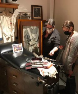 Two masked women behind a museum display of medical equipment